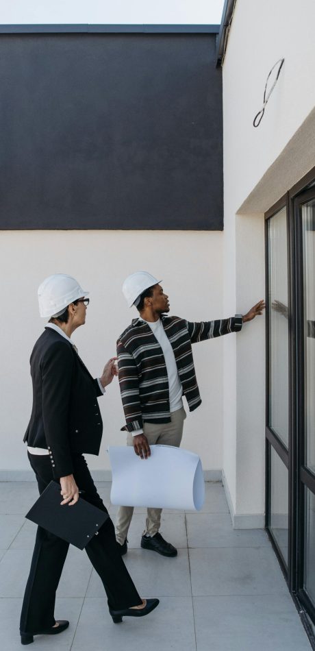 Two architects in hard hats discussing a modern building's glass facade.